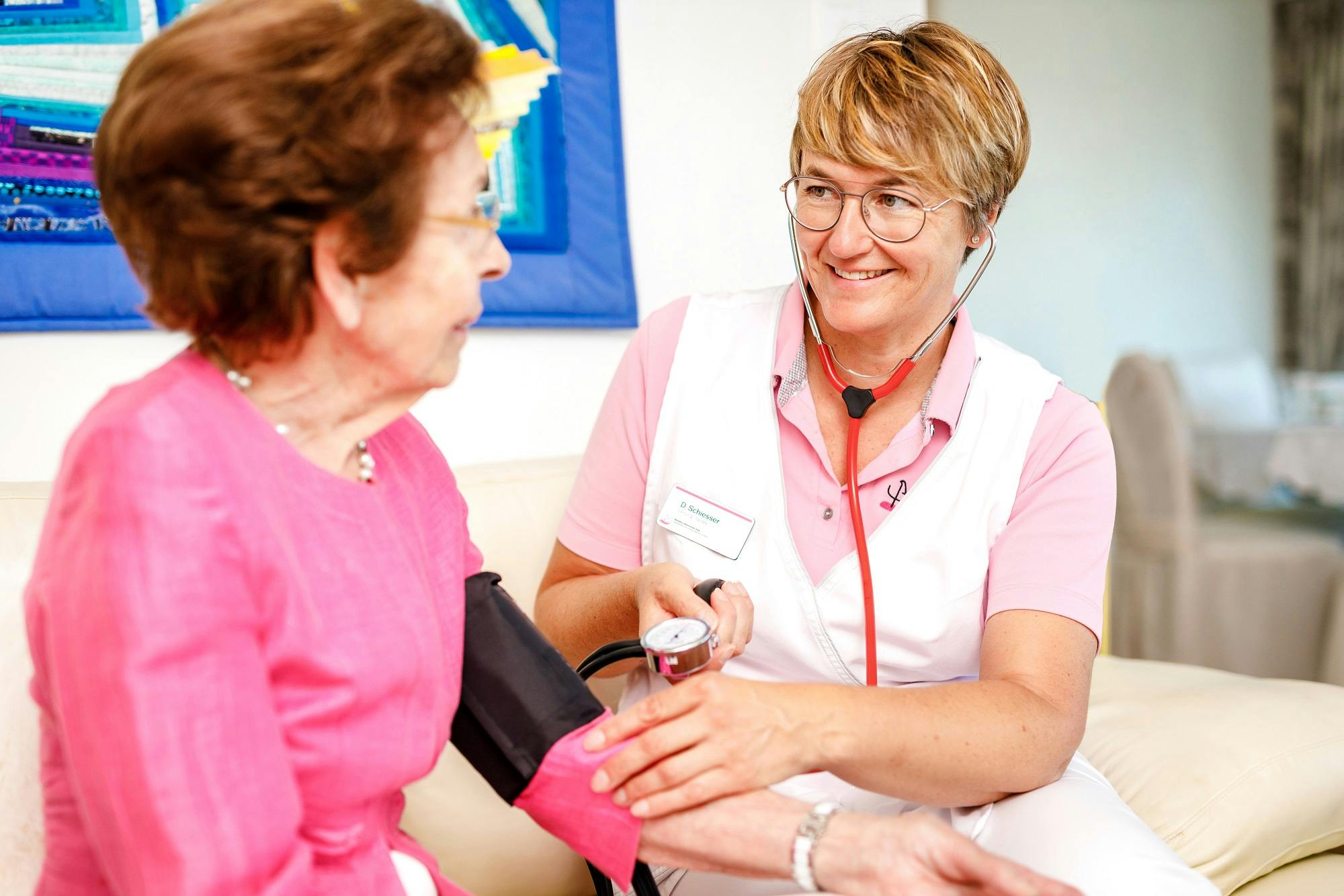 Ältere Frau erhält Blutdruckmessung von lächelnder medizinischer Fachkraft.
