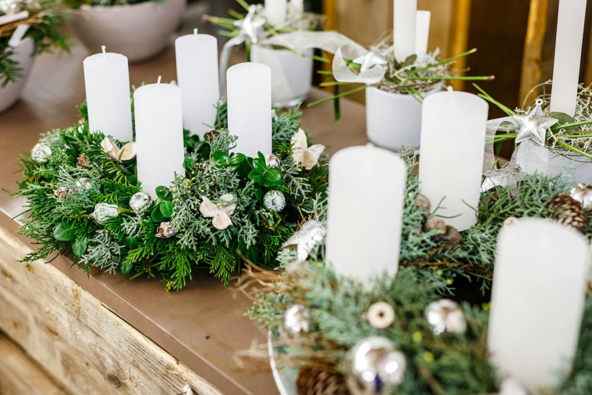 Adventskranz mit weißen Kerzen und weihnachtlicher Dekoration aus Tannenzweigen und Kugeln.
