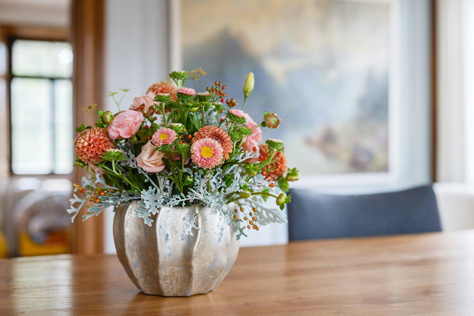 Bunter Blumenstrauß in einer silbernen Vase auf einem Holztisch, interieurbezogener Hintergrund.