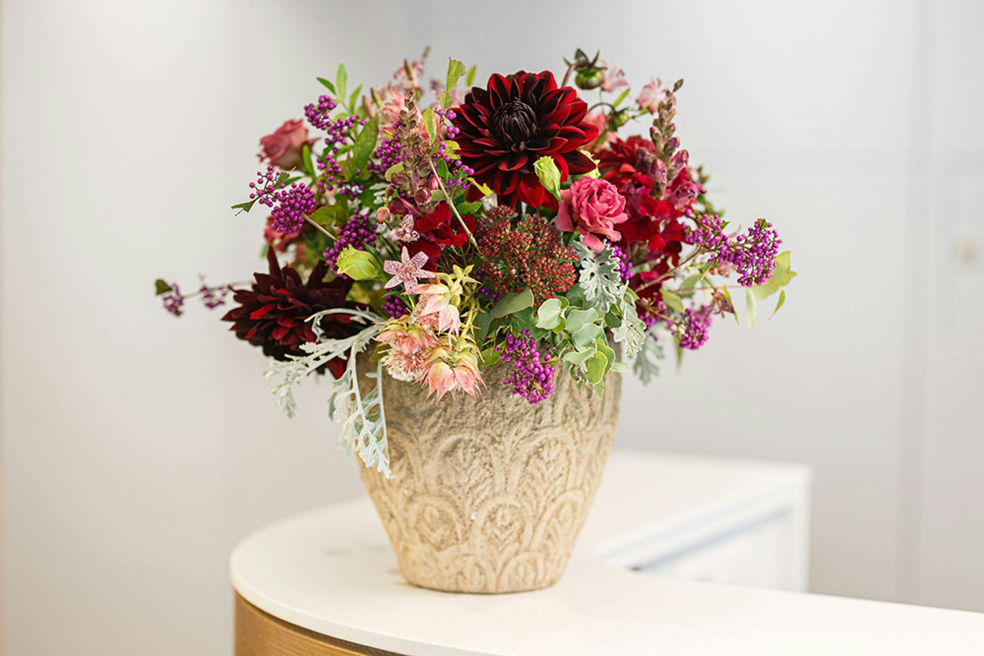 Blumenstrauß mit roten und violetten Blumen in einer verzierten Vase auf einem Tisch.
