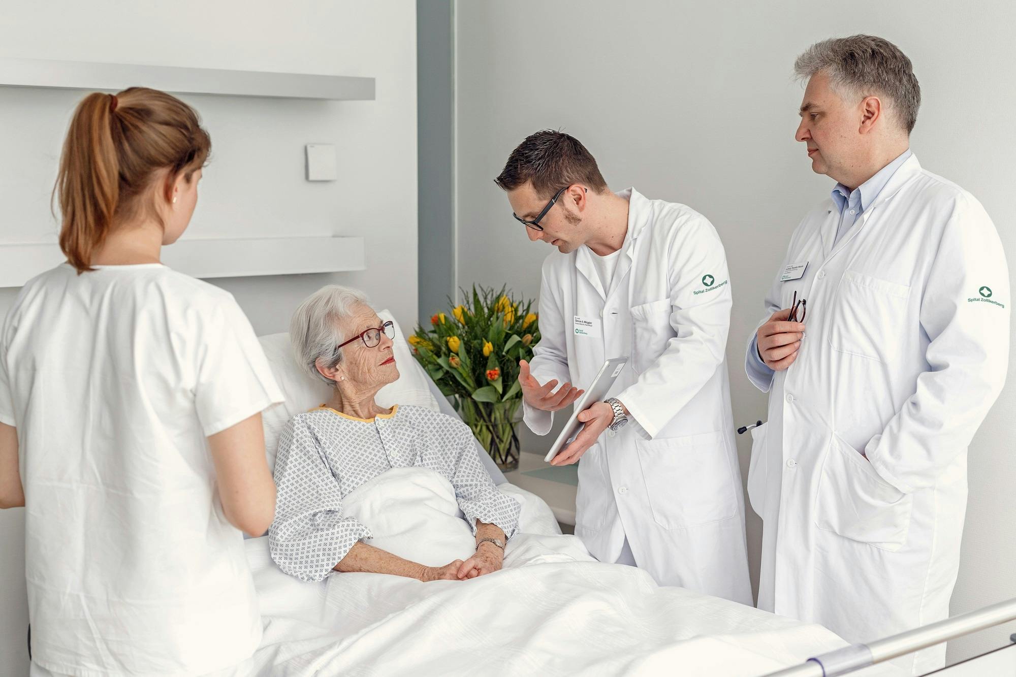 "Ältere Patientin im Krankenhausbett im Gespräch mit medizinischem Personal"