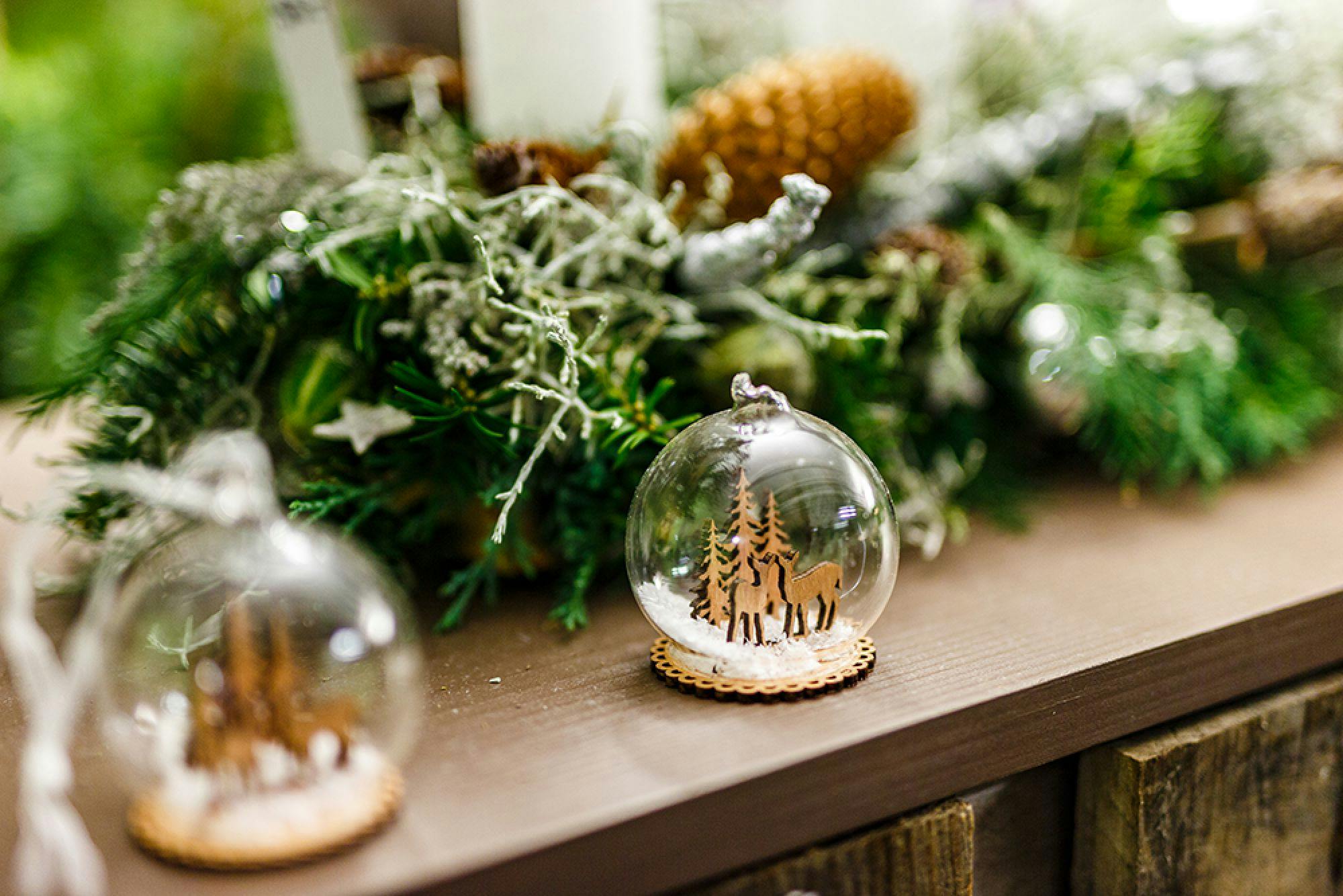 Weihnachtliche Tischdekoration mit einer Glaskugel, in der ein Miniatur-Waldmotiv zu sehen ist, umgeben von Kerzen und Tannenzapfen.