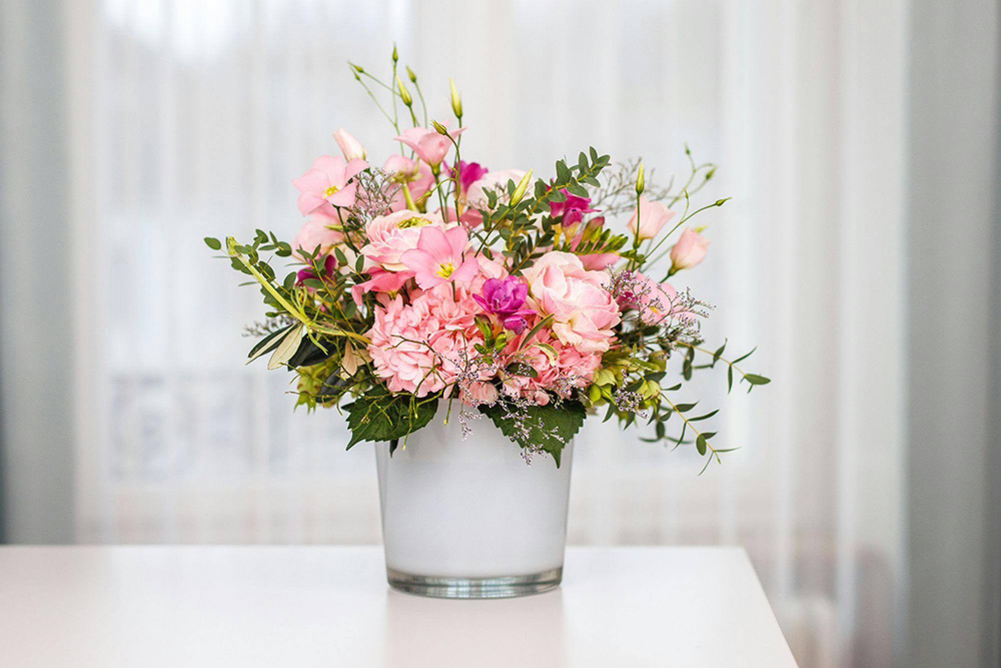 Farbenfroher Blumenstrauß aus rosa Blüten in einer Vase, vor einem hellen Hintergrund.